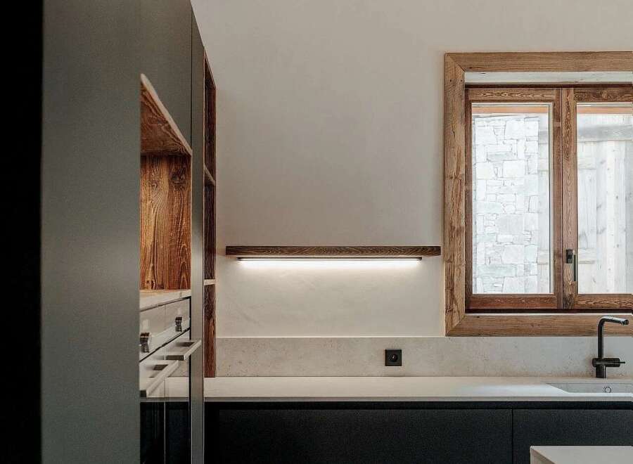 Experience modern rustic charm in this stunning kitchen, featuring sleek dark cabinetry contrasted with warm, exposed wooden beams on the ceiling and a rustic wooden window frame.