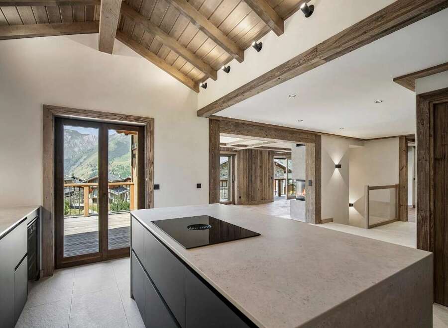 Experience luxury mountain living in this stunning chalet-style kitchen, featuring a sleek island with a built-in stovetop and breathtaking panoramic views of the Alps.