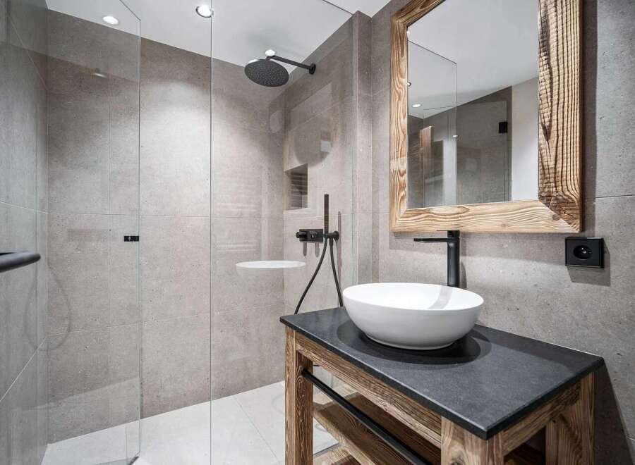 Experience modern luxury in this stunning bathroom featuring a spacious walk-in shower with a rainfall showerhead and sleek grey tilework.