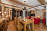 Experience luxurious alpine living in this stunning dining and living area, featuring a grand wooden dining table set for a feast and plush red seating arranged around a cozy stone fireplace.