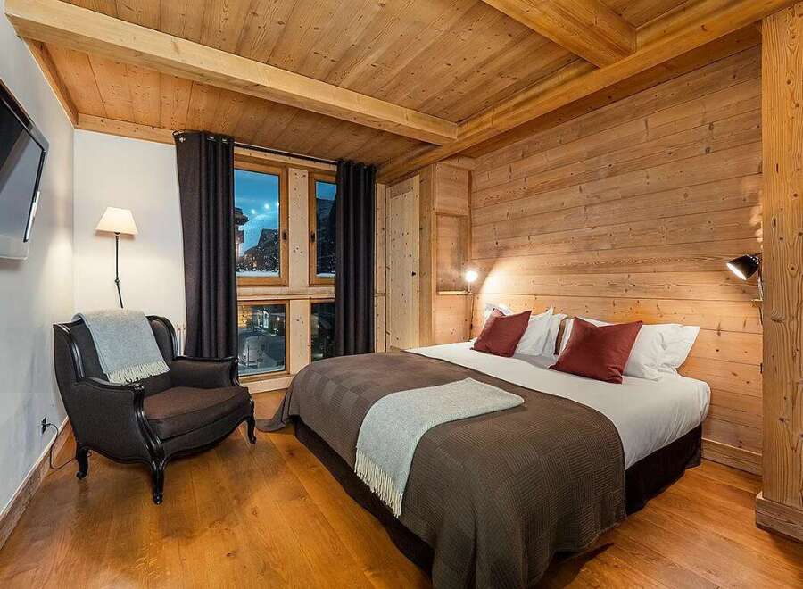 Experience cozy mountain living in this charming bedroom featuring warm wood paneling and exposed beams.