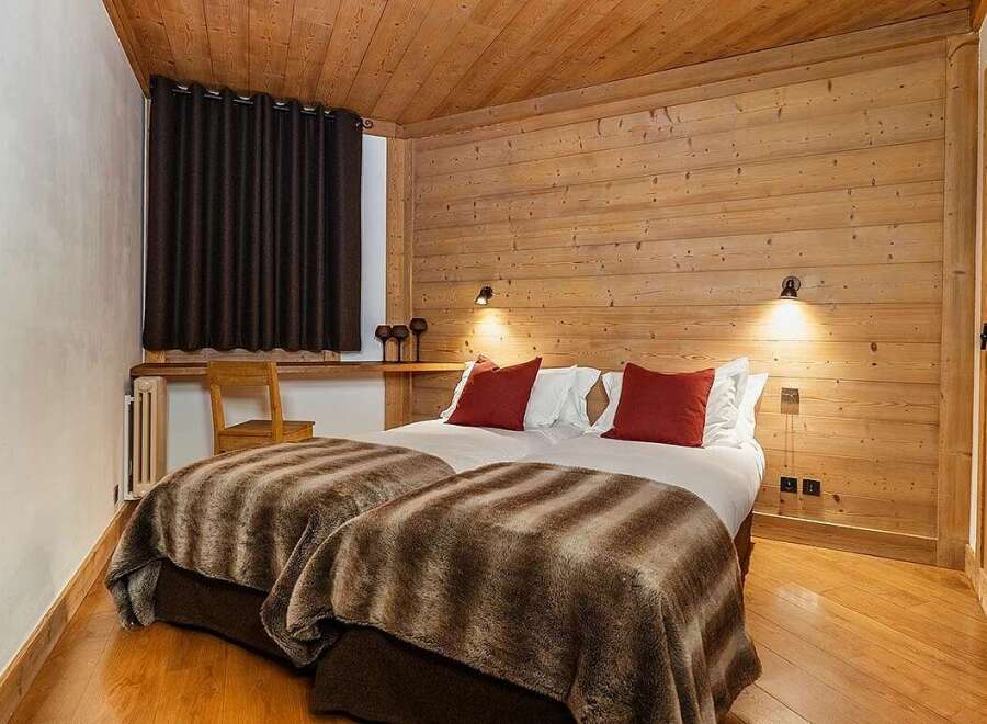 Experience cozy mountain living in this charming bedroom featuring two comfortable beds adorned with plush, striped throws and vibrant red accent pillows.