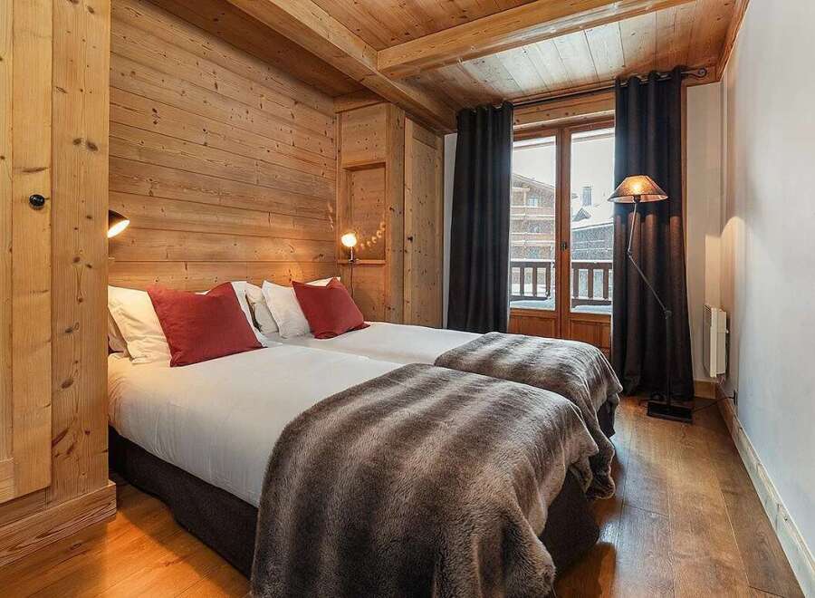 Experience cozy mountain living in this charming bedroom featuring two comfortable twin beds adorned with plush red pillows and soft, faux fur throws.