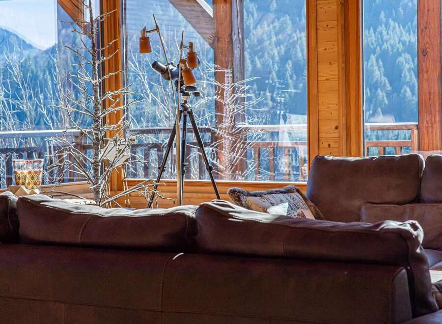 Experience breathtaking mountain views from this cozy living room, featuring a large telescope perfect for stargazing or wildlife observation.