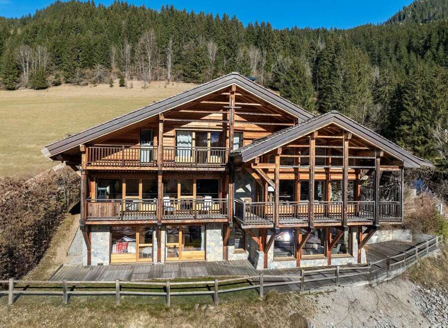 Experience luxury mountain living in this stunning chalet, featuring expansive wooden balconies and large windows that offer breathtaking forest views.