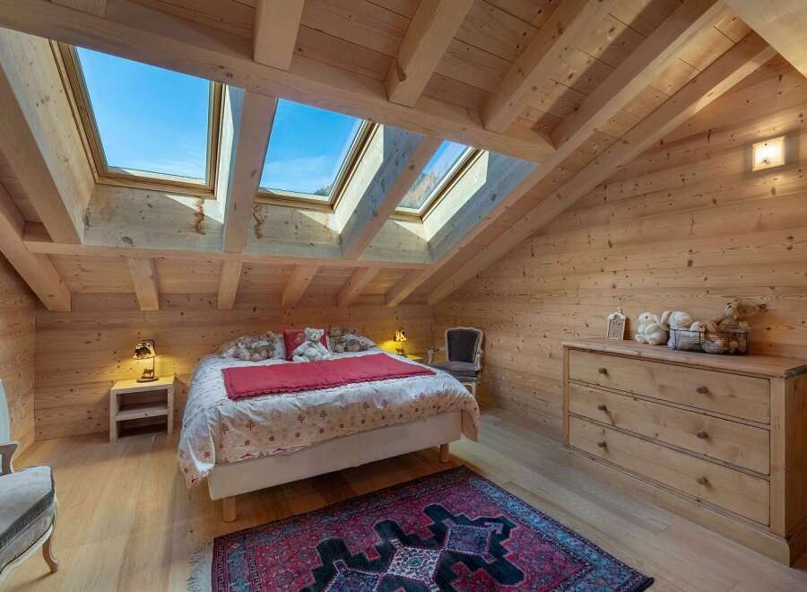 Experience cozy mountain living in this charming attic bedroom, featuring a comfortable bed adorned with plush teddy bears and a vibrant red throw.