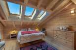 Experience cozy mountain living in this charming attic bedroom, featuring a comfortable bed adorned with plush teddy bears and a vibrant red throw.