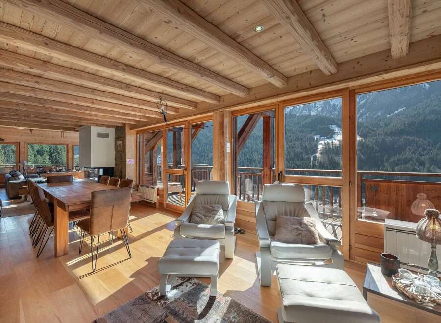Experience breathtaking mountain views from this luxurious chalet living space, featuring a rustic wooden ceiling and exposed beams.