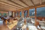 Experience breathtaking mountain views from this luxurious chalet living space, featuring a rustic wooden ceiling and exposed beams.