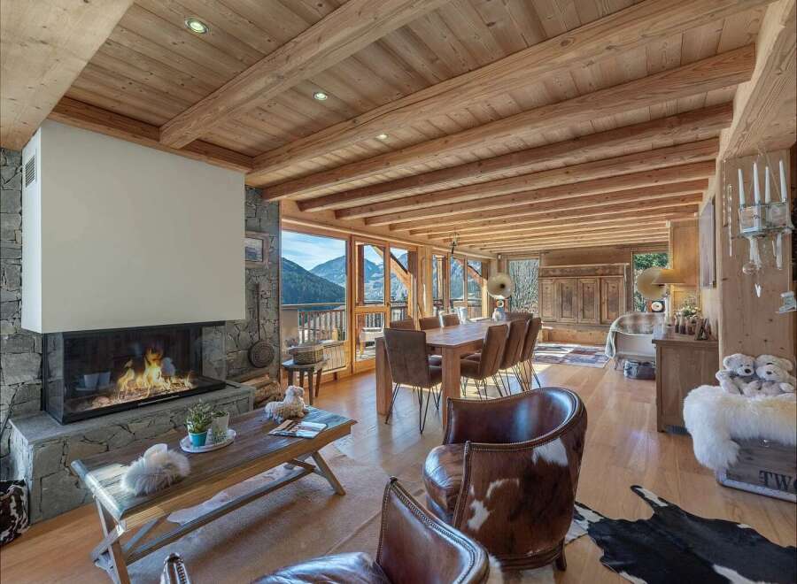Experience rustic luxury in this stunning mountain chalet, featuring a grand stone fireplace and exposed wooden beams that create a warm and inviting atmosphere.