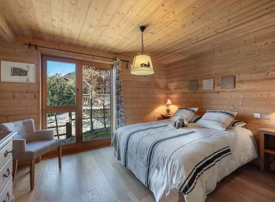 Experience cozy mountain living in this charming chalet bedroom, featuring warm wooden paneling throughout and a comfortable queen-sized bed adorned with striped linens.