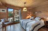 Experience cozy mountain living in this charming chalet bedroom, featuring warm wooden paneling throughout and a comfortable queen-sized bed adorned with striped linens.