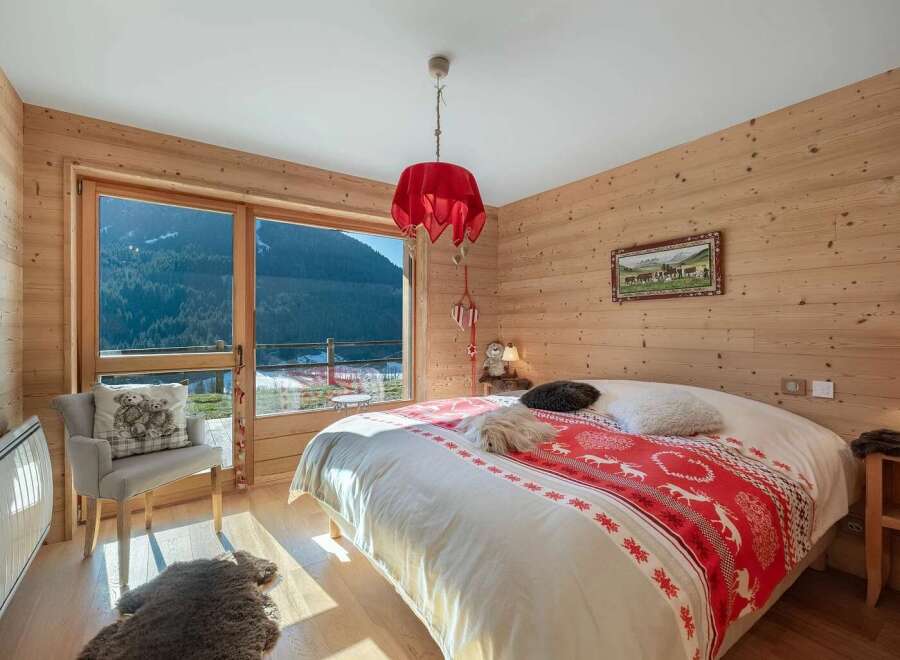 Experience cozy mountain living in this charming bedroom featuring warm wood paneling and a large window with breathtaking alpine views.