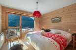Experience cozy mountain living in this charming bedroom featuring warm wood paneling and a large window with breathtaking alpine views.