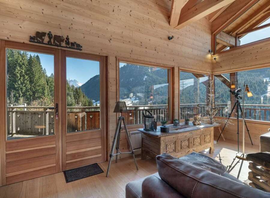Experience breathtaking mountain views from this stunning chalet living room, featuring expansive windows and a rustic wooden interior.