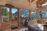 Experience breathtaking mountain views from this stunning chalet living room, featuring expansive windows and a rustic wooden interior.