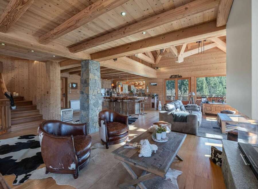 Experience rustic luxury in this stunning log cabin living space, featuring exposed wooden beams and a grand stone fireplace.