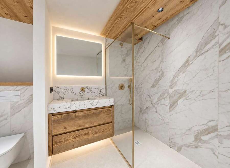 Experience luxury in this modern bathroom featuring a stunning marble-tiled shower with a sleek glass enclosure and gold fixtures.