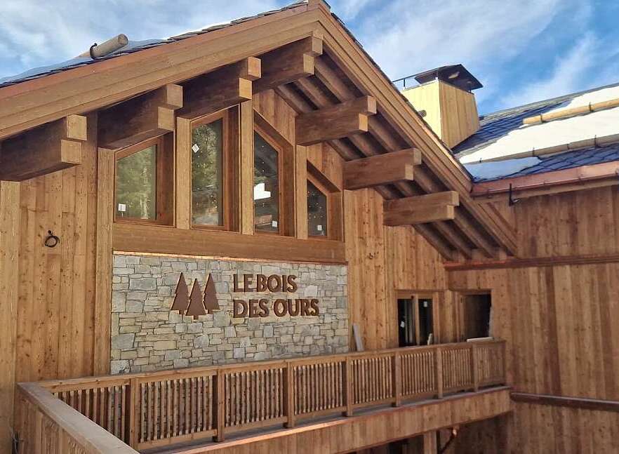 Experience the charm of this rustic wooden chalet, featuring a stone facade with the 'Le Bois Des Ours' inscription.