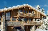Experience luxury mountain living in this stunning chalet, featuring a rustic stone and wood exterior nestled amidst snow-covered pine trees.
