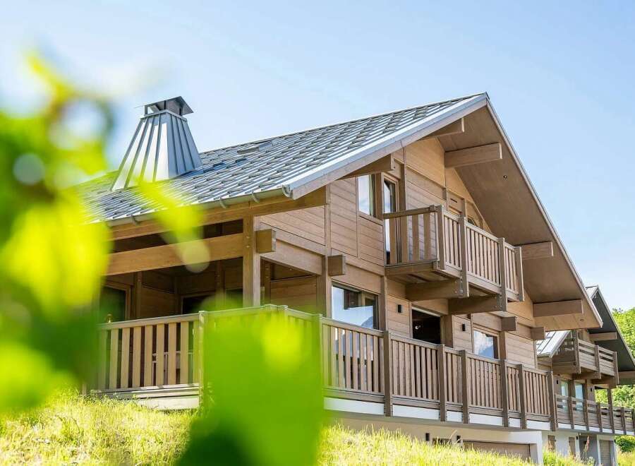 Experience luxury mountain living in this stunning wooden chalet, featuring a modern metal roof and a prominent chimney.