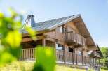 Experience luxury mountain living in this stunning wooden chalet, featuring a modern metal roof and a prominent chimney.