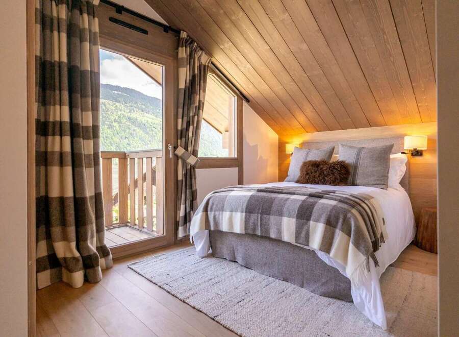 Experience cozy mountain living in this charming bedroom, featuring a comfortable bed adorned with a classic plaid blanket and plush pillows.