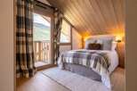 Experience cozy mountain living in this charming bedroom, featuring a comfortable bed adorned with a classic plaid blanket and plush pillows.