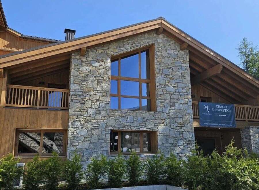 Experience luxury living in this stunning chalet, featuring a striking stone facade and expansive wooden beams.