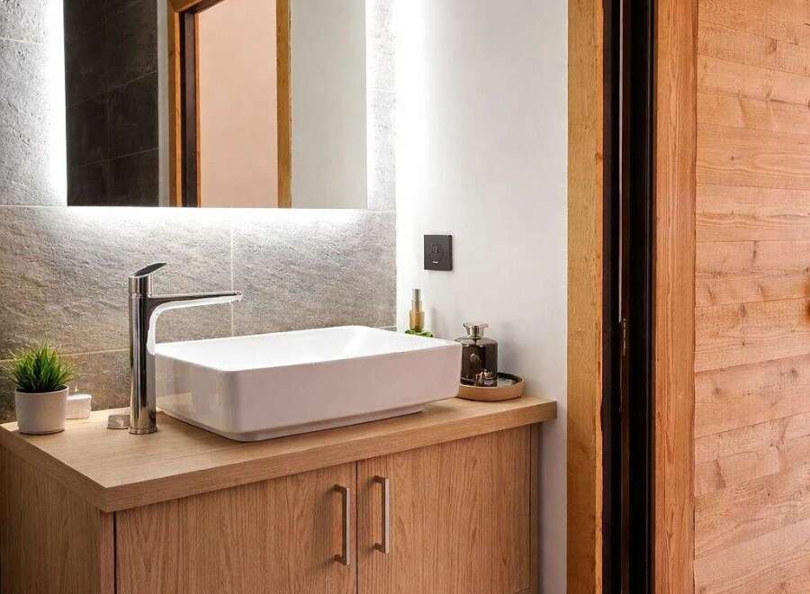 This modern bathroom features a sleek white vessel sink atop a warm oak vanity with ample storage.
