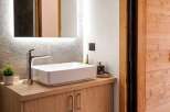 This modern bathroom features a sleek white vessel sink atop a warm oak vanity with ample storage.