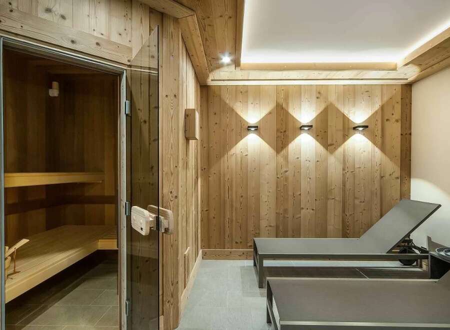 Experience ultimate relaxation in this luxurious spa area, featuring a traditional wooden sauna with glass doors and comfortable lounge chairs.