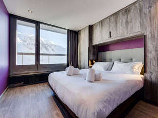 Experience luxury mountain living in this stunning bedroom, featuring a plush king-size bed and breathtaking panoramic views of snow-capped mountains through expansive windows.
