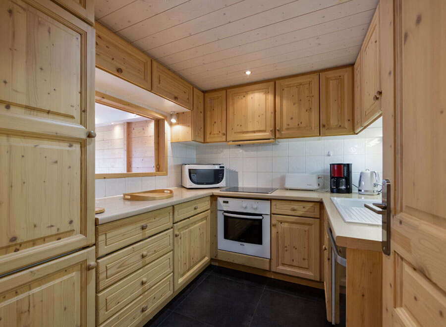 This charming kitchen features warm, natural wood cabinetry and a pass-through window, creating a cozy and inviting atmosphere.