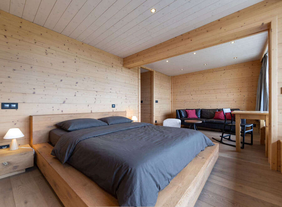 Experience rustic luxury in this charming wooden bedroom, featuring a comfortable bed with dark grey linens and a matching nightstand with a modern lamp.