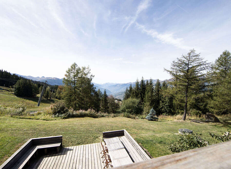 Enjoy breathtaking mountain views from this stunning property's expansive wooden deck, perfect for outdoor dining and relaxation.