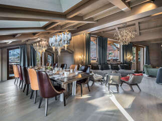 Experience luxurious mountain living in this stunning dining and living area, featuring a grand wooden dining table set for a feast and elegant chandeliers that illuminate the space.