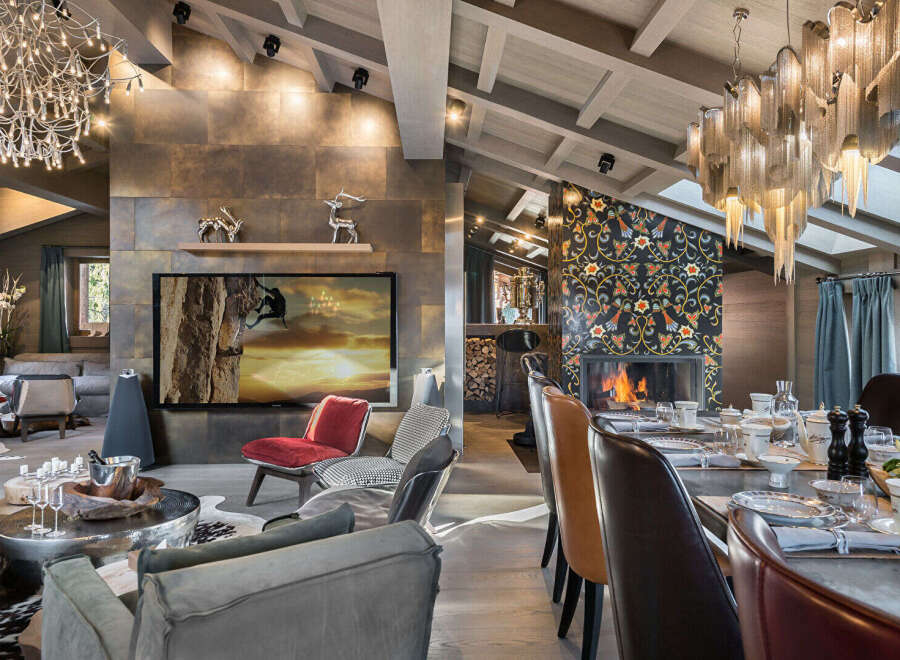Experience luxury living in this stunning mountain retreat, featuring a spacious open-plan living area with a modern fireplace and a large flat-screen TV displaying a dramatic climbing scene.