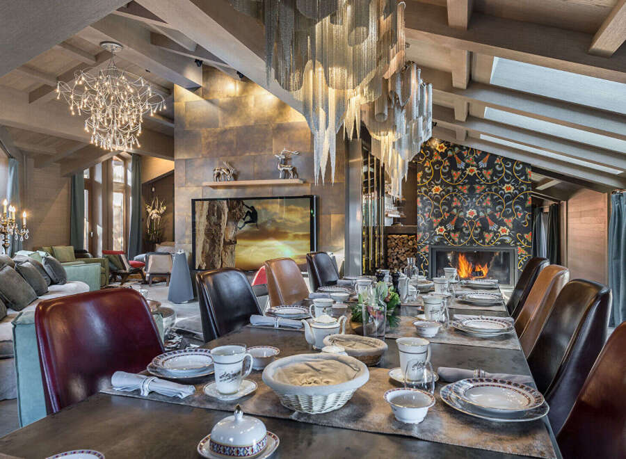 Experience luxurious mountain living in this stunning dining room, featuring a grand fireplace with intricate tilework and a dramatic multi-tiered chandelier.