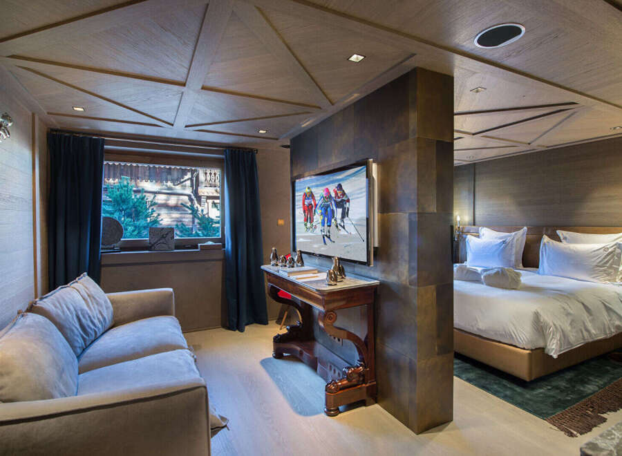 Experience luxury mountain living in this beautifully appointed suite, featuring a plush sofa and a large flat-screen TV displaying vibrant ski imagery.