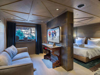 Experience luxury mountain living in this beautifully appointed suite, featuring a plush sofa and a large flat-screen TV displaying vibrant ski imagery.