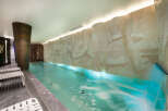 Experience ultimate relaxation in this luxurious indoor pool area, featuring a stunning rock-like wall with integrated waterfall and soothing blue lighting.