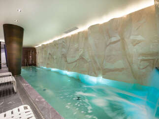 Experience ultimate relaxation in this luxurious indoor pool area, featuring a stunning rock-like wall with integrated waterfall and soothing blue lighting.
