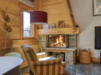 Cozy up by the stone fireplace in this charming living room, featuring warm wooden walls and a comfortable striped armchair.