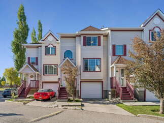 Discover this charming townhouse complex featuring a row of beige townhouses with burgundy accents and white garages.