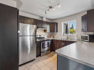 This spacious kitchen features dark wood cabinetry, stainless steel appliances including a refrigerator and range, and a double sink with a window overlooking a lush, green backyard.