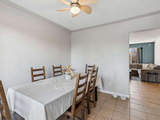 This dining area features a charming wooden table set with a light-colored tablecloth and decorative placemats, complemented by six matching wooden chairs.