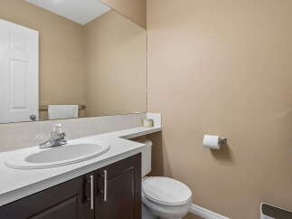 This powder room features a sleek vanity with a white countertop and dark wood cabinets, complemented by a modern chrome faucet and a large mirror.