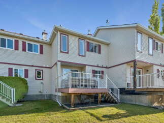 This multi-story townhouse features a light beige exterior with dark red trim and shutters, offering a classic and inviting look.