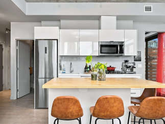 Experience modern urban living in this stylish condo kitchen, featuring sleek white cabinetry, a stainless steel refrigerator, and a convenient microwave.